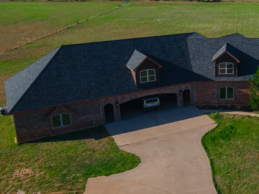 Dark shingle roof with two dormers over a brick garage wing
